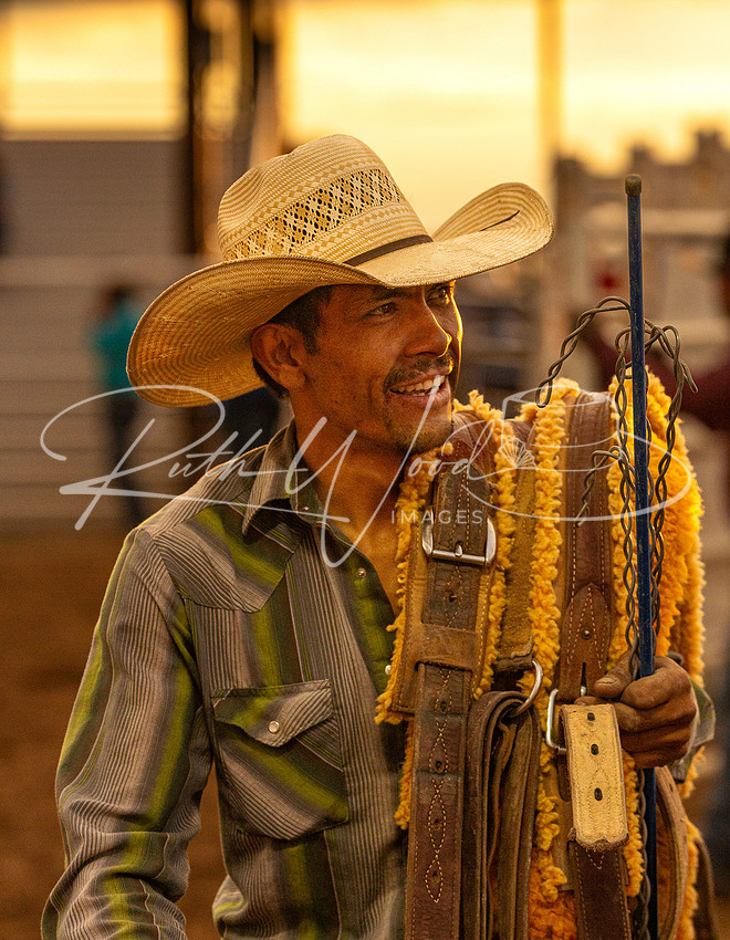 Smiling cowboy in a straw hat holding his rigging in warm light