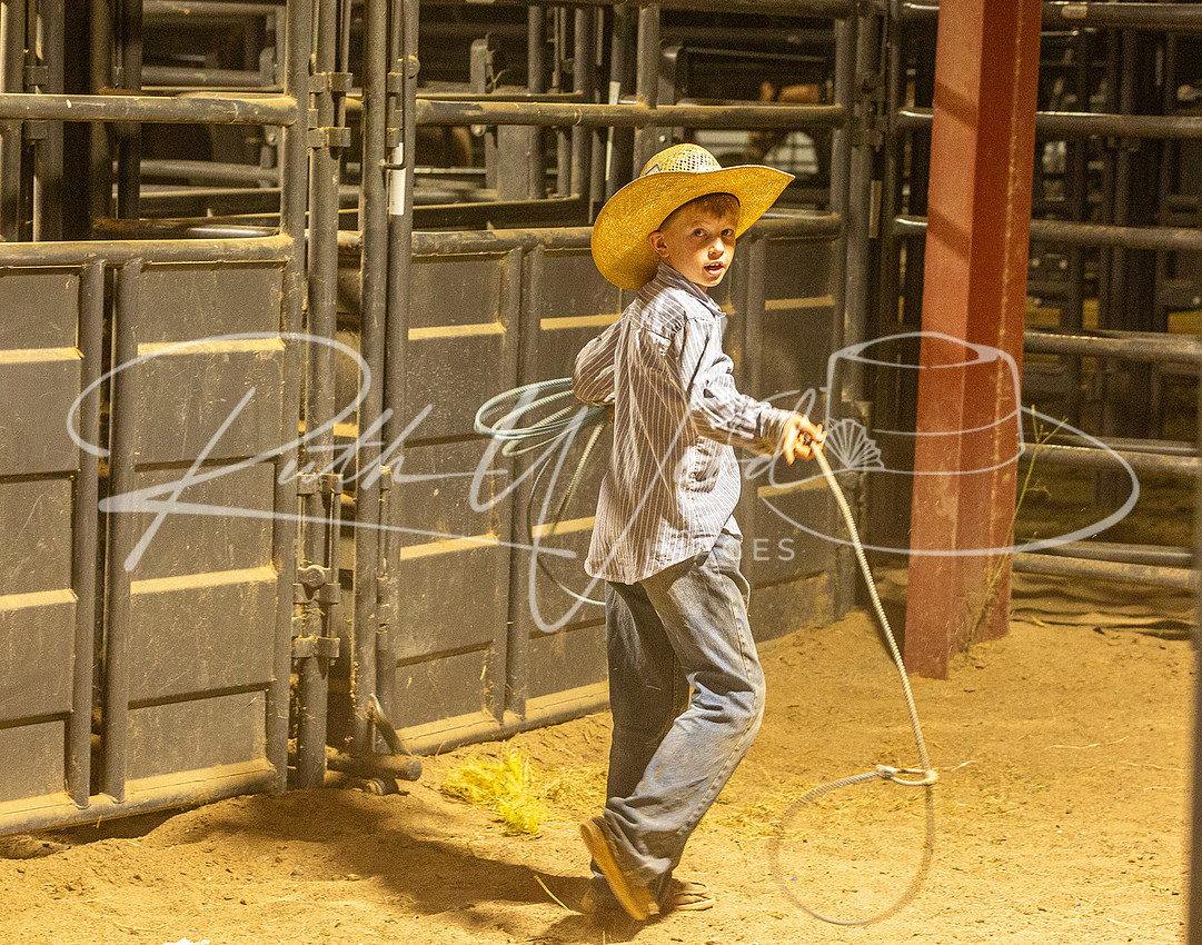 Young cowboy in a yellow hat swinging a rope by the pens